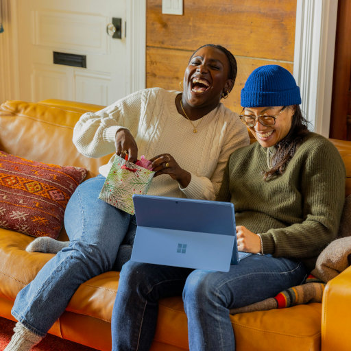 Two women are sitting together on a leather couch looking at a laptop.